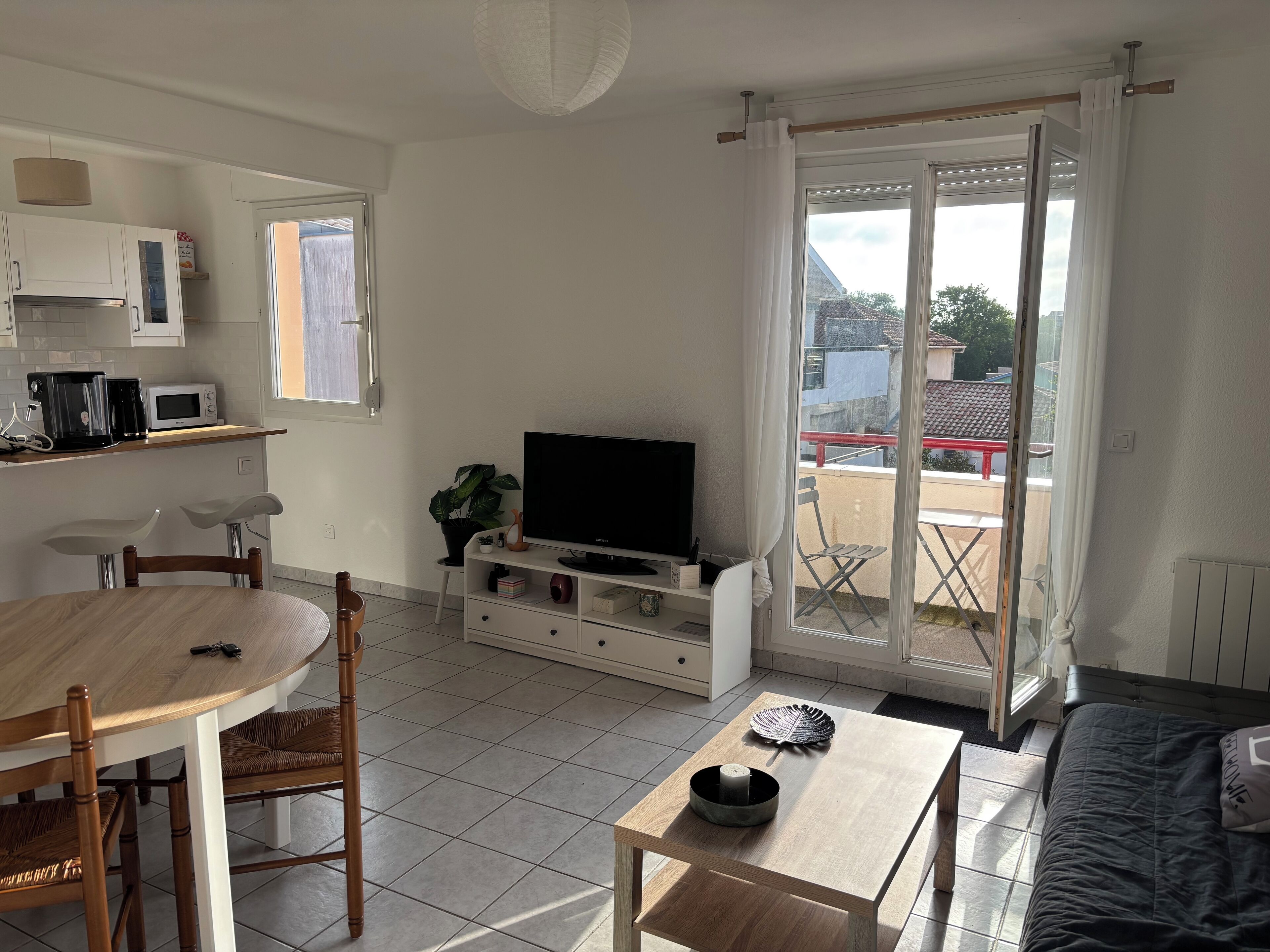 A living room with a TV, dining table, chairs, and a balcony with a view.