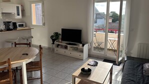 Ett vardagsrum med TV, matbord, stolar och en balkong med utsikt.