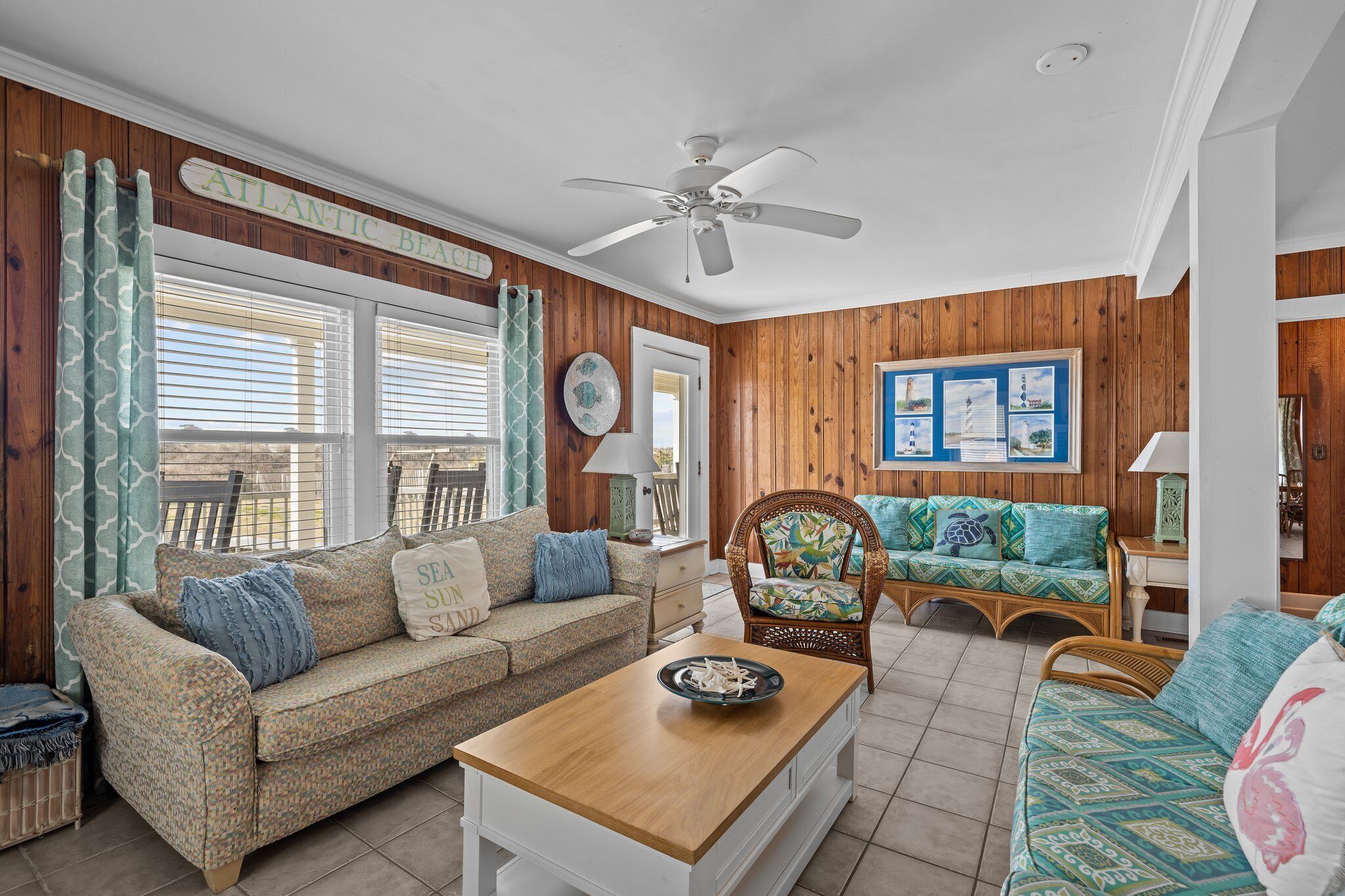 A cozy living room with a wooden paneled wall, a ceiling fan, and a view of the outdoors through large windows.