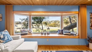 Ein Zimmer mit großem Fenster, einem weißen Sofa und Blick auf einen Park.