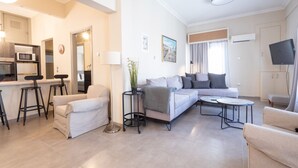 A modern living room with a sofa, two round coffee tables, a small side table with a plant, and a kitchen area with a microwave and bar stools. - Kastella Waves Chic 2-bedroom Getaway w sea View (Piraeus)