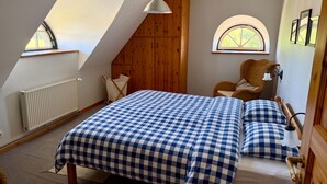 Un dormitorio con una colcha a cuadros, una silla de madera, un radiador y una ventana con vistas.