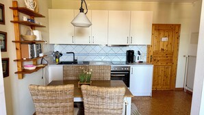 Una cocina con isla central, sillas de mimbre, lámpara colgante y estantes de madera.