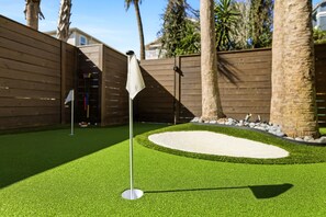 A miniature golf course with a green artificial turf, a sand trap, and a wooden fence in the background. - Luxury Townhouse | Steps to Beach + Golf Cart (Jacksonville Beach)
