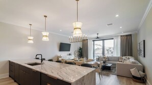 A modern kitchen with a marble island, pendant lights, and a dining area with a sofa and coffee table.