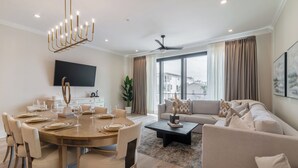A modern living room with a dining area, a flat-screen TV, a ceiling fan, and large windows with curtains.