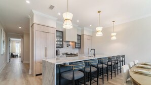 A modern kitchen with a marble island, bar stools, pendant lighting, and a dining area with a round table.