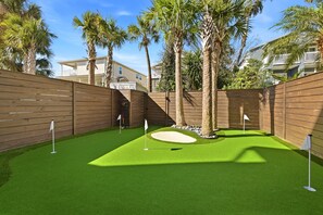 A backyard with artificial green turf, a sand bunker, and a wooden fence. - Luxury Townhouse | Steps to Beach + Golf Cart (Jacksonville Beach)