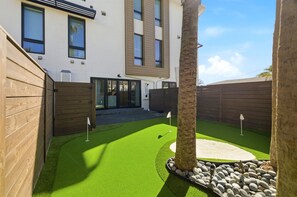 A modern house with a well-maintained lawn, a wooden fence, and a palm tree. - Luxury Townhouse | Steps to Beach + Golf Cart (Jacksonville Beach)