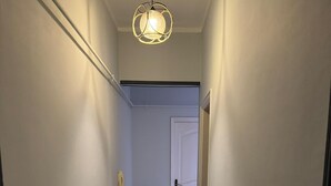 Un couloir étroit aux murs blancs et au sol carrelé, qui mène à une porte au fond.