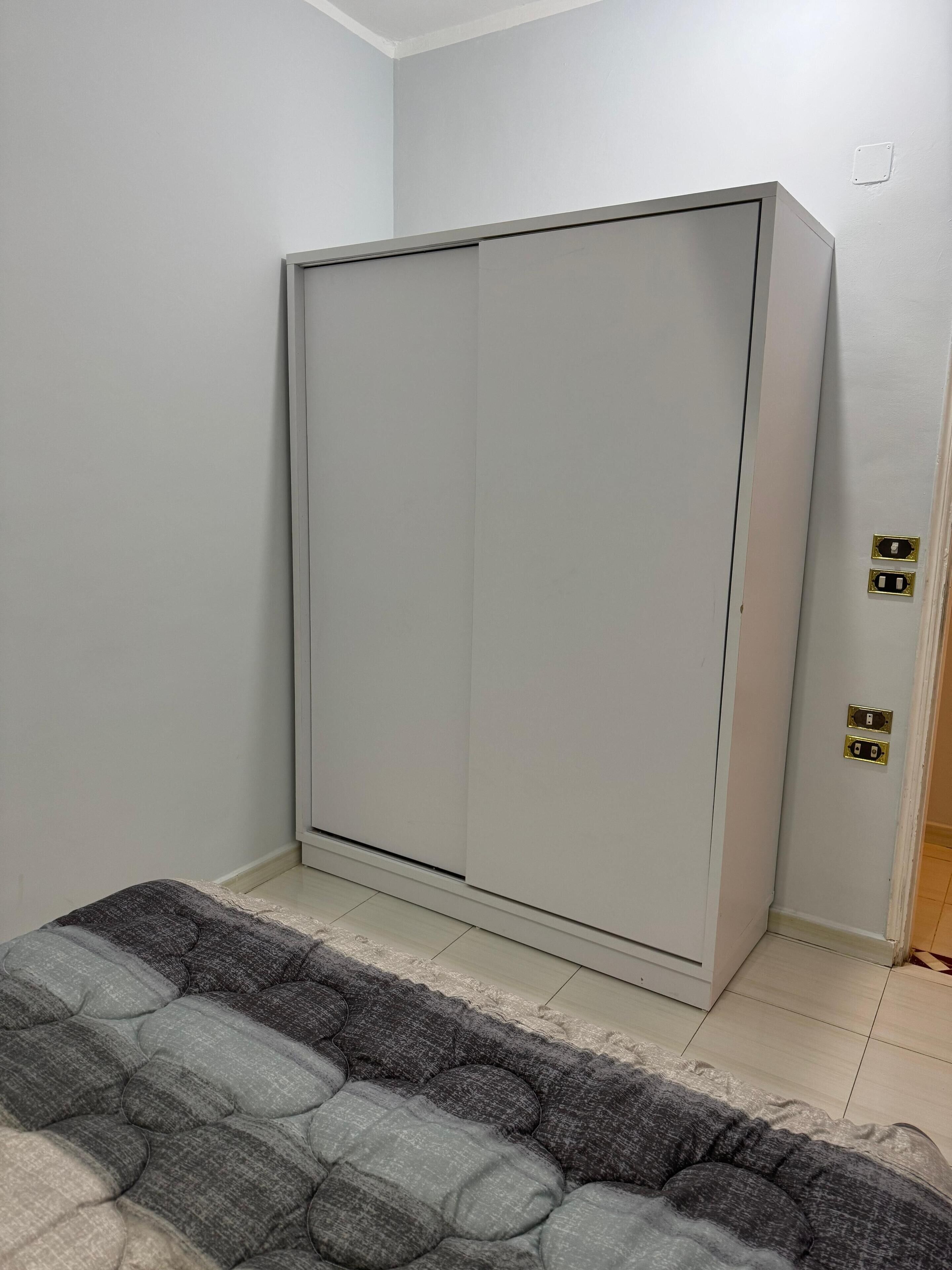 A bedroom with a bed, a wardrobe, and a door with electrical outlets.
