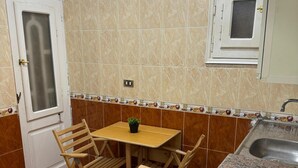 Une cuisine de taille réduite avec un carrelage à motifs, une petite table à manger avec des chaises, un évier et une fenêtre donnant sur un beau paysage.