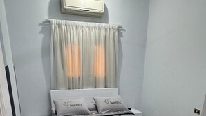 Une chambre à coucher comprenant un lit, une table de chevet, une commode, un radiateur et une fenêtre avec des rideaux.