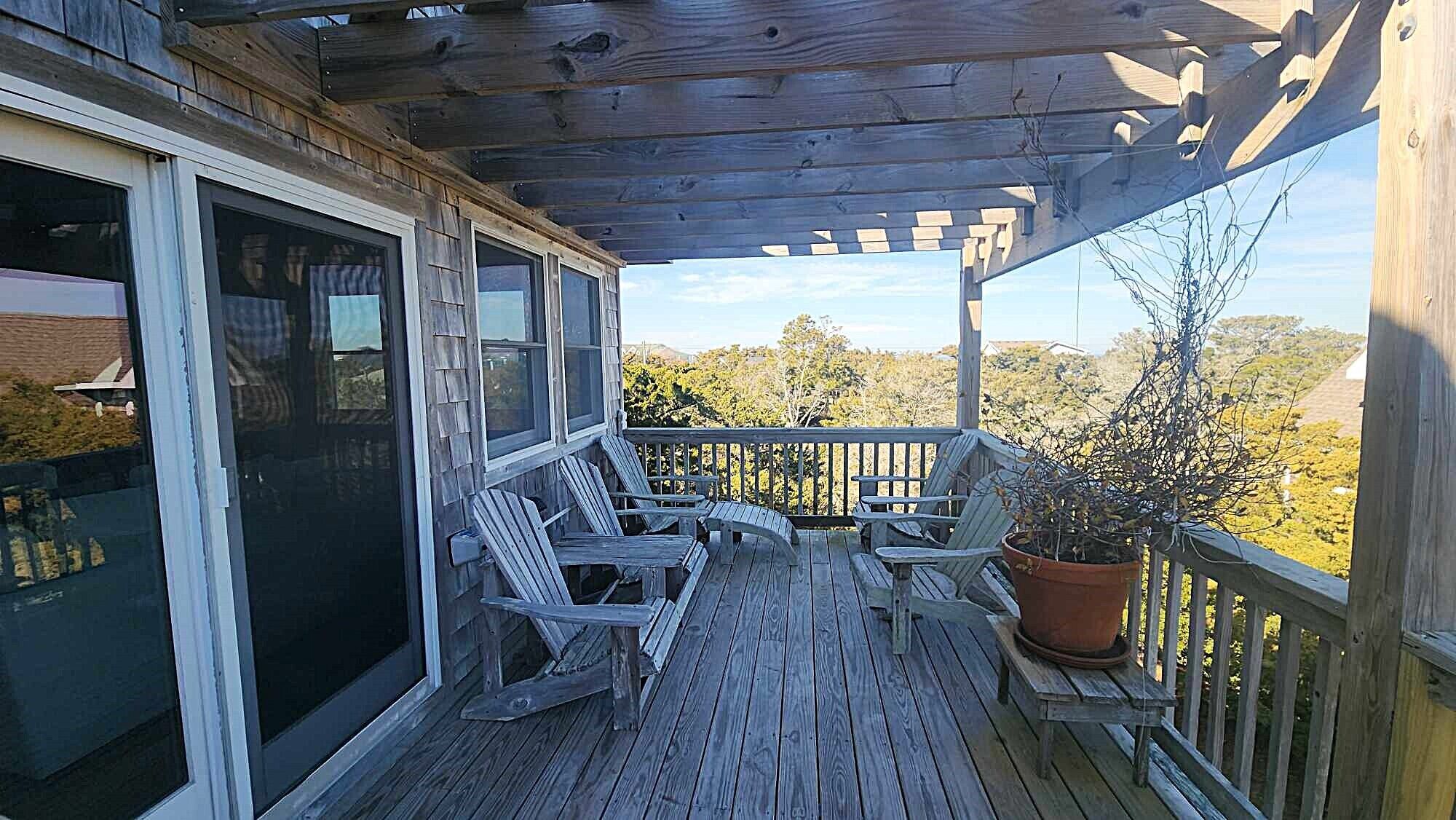 Une terrasse en bois avec des chaises Adirondack et une plante en pot.