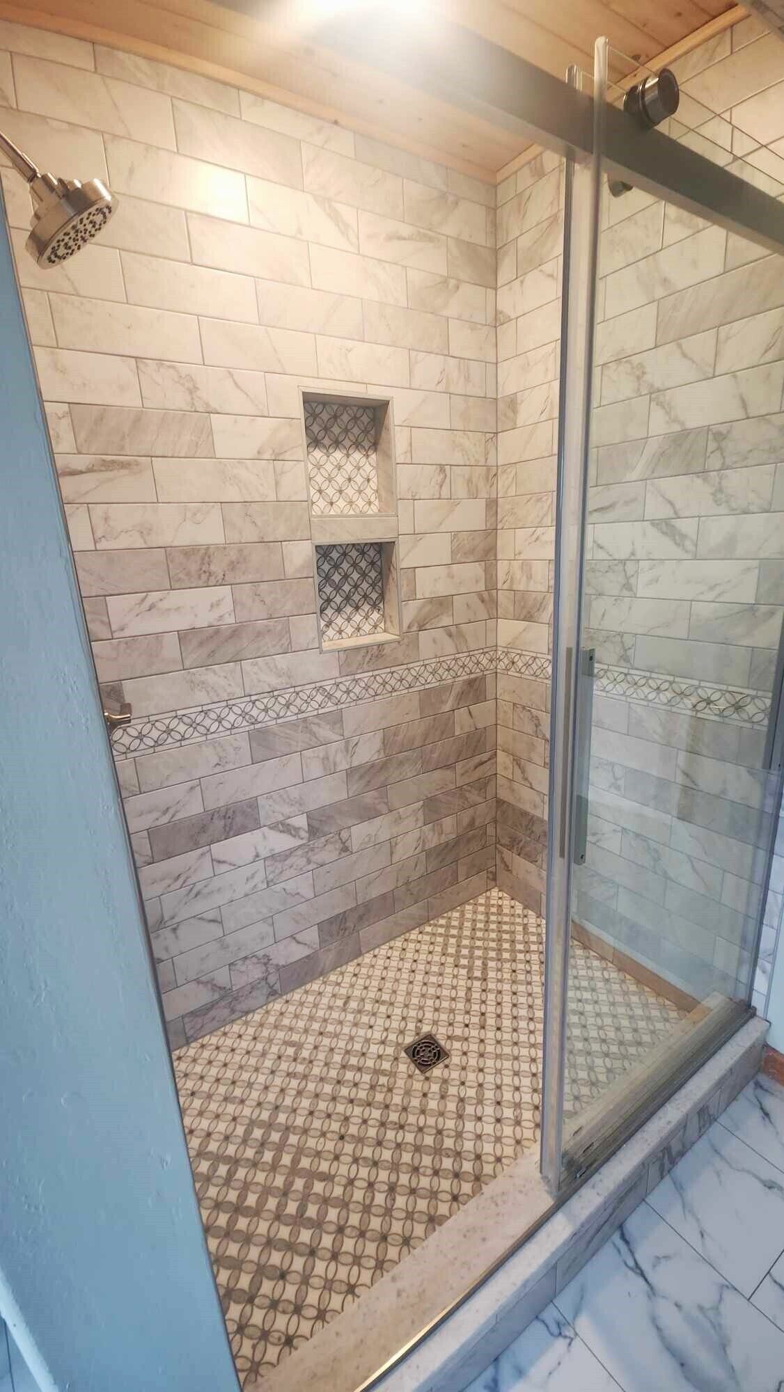A shower area with a glass door, marble tiles, and a patterned floor.