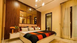 A modern bedroom with a large bed, a bedside table with a vase of flowers, a mirror, and a view of the bathroom. - Premium Service Flats (Kharar)