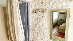 Una habitación con pared de piedra rústica, puerta de madera, espejo y suelo de baldosas.