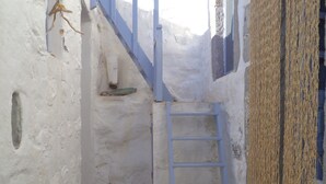 Un pasillo estrecho, con paredes blancas y una escalera azul que lleva a una puerta.