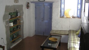 Una habitación con una puerta azul, una ventana decorada con una luna creciente, una estantería con libros y un pequeño calentador, y un sofá a rayas.