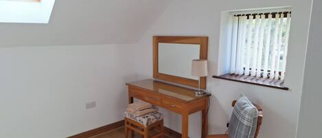 A bedroom with a wooden dresser, a mirror, a small table, a chair, and a window with curtains.