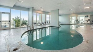 An indoor swimming pool with clear glass walls, a tiled floor, and a few lounge chairs.