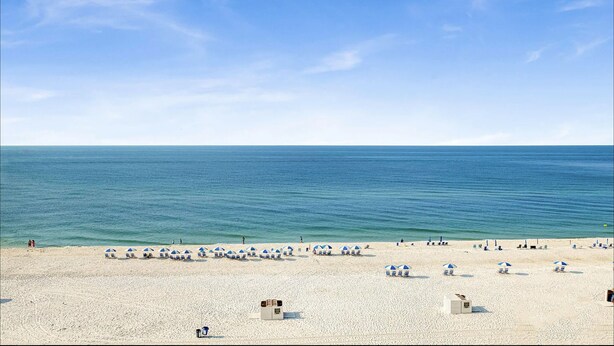 A beach with rows of blue and white beach umbrellas, a lifeguard tower, and a clear view of the ocean.