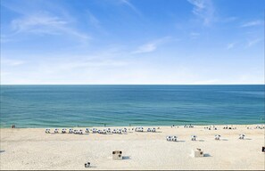 A beach with rows of blue and white beach umbrellas, a lifeguard tower, and a clear view of the ocean.