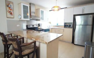 Una cocina moderna con una isla central, electrodomésticos de acero inoxidable y un comedor con dos sillas.