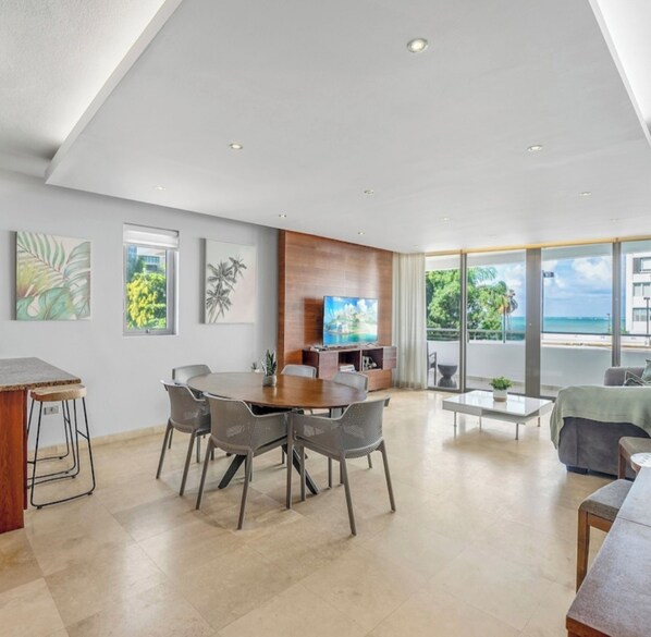 A modern living room with a dining area, large windows, and a view of the outdoors. - Oceanside Adventures (C. Avenue Boca de Cangrejos)