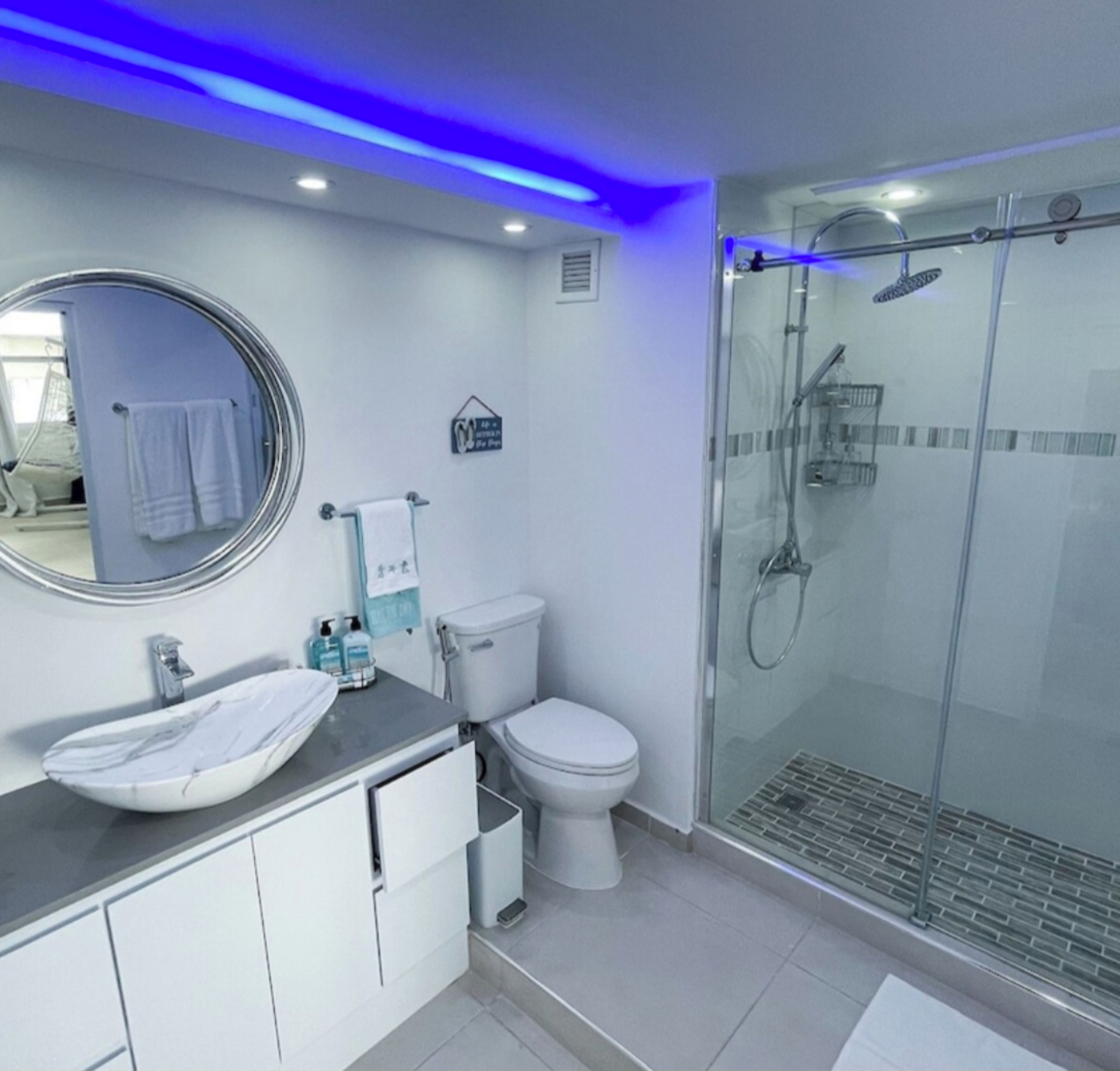 A modern bathroom with a glass shower enclosure, a white sink with a marble basin, and a toilet.