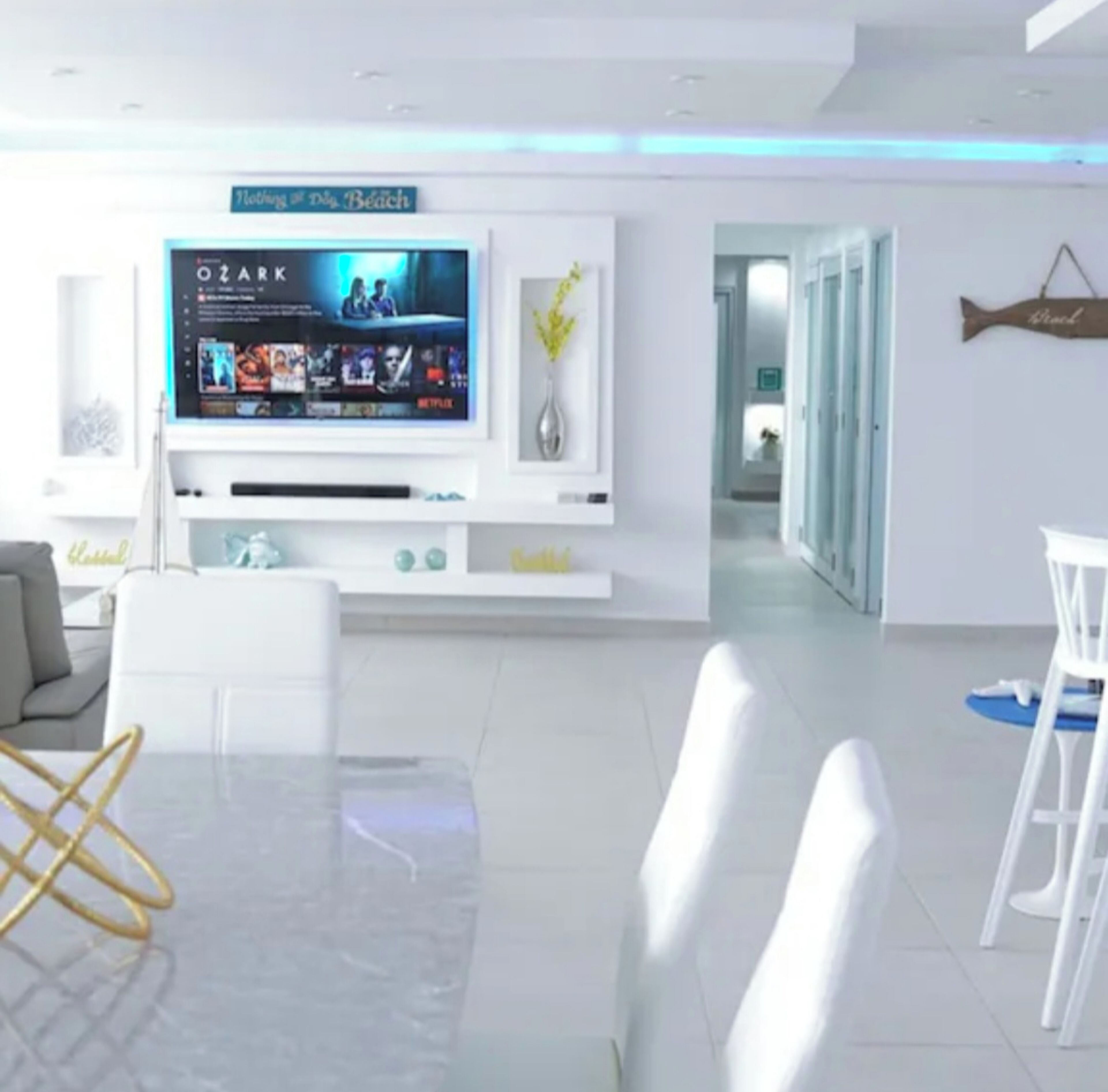A modern living room with a flat-screen TV, white furniture, and a sign reading 'Nothing but the Beach.'