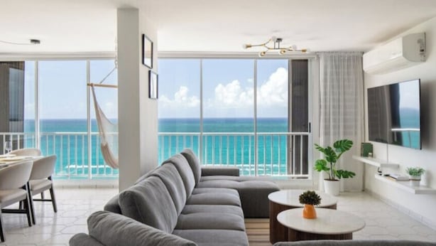 Een moderne woonkamer met een ruime bank, een eethoek en een balkon met uitzicht op zee.