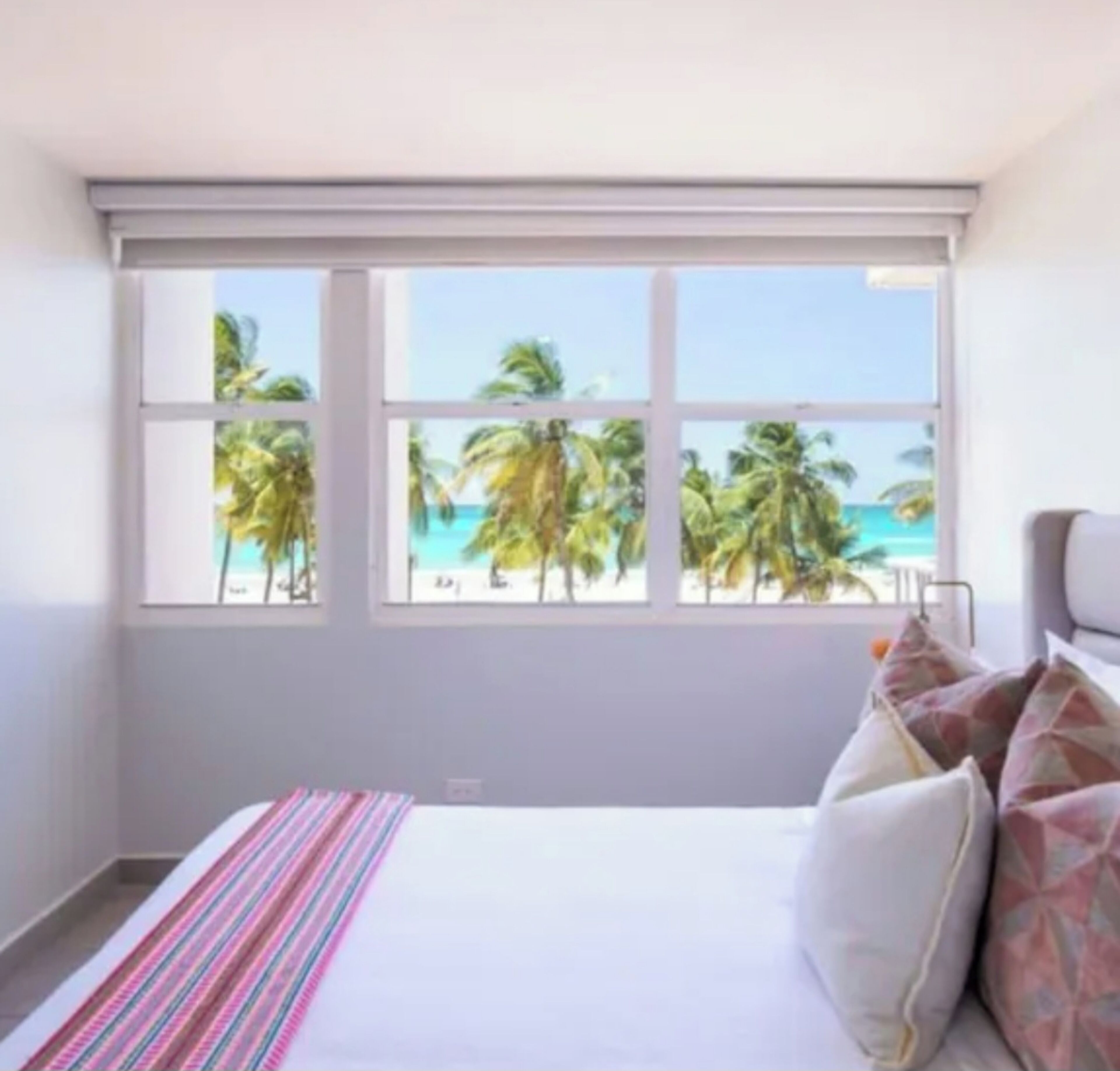 Une chambre avec une grande fenêtre, un lit et une vue sur les palmiers et la mer.