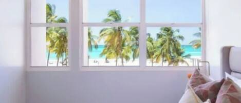 Une chambre avec une grande fenêtre, un lit et une vue sur les palmiers et la mer.