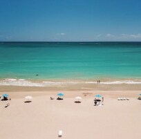 Una playa con agua turquesa cristalina, algunas personas y varios sombrillas.