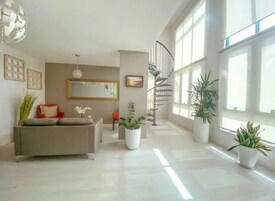 Un amplio salón con una escalera moderna, ventanas grandes y una paleta de colores neutros.
