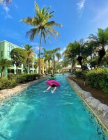 Una piscina con acqua cristallina, circondata da palme e un edificio con bordo piscina piastrellato.