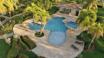 Una gran piscina al aire libre con varias secciones, rodeada de palmeras y jardines bien cuidados.