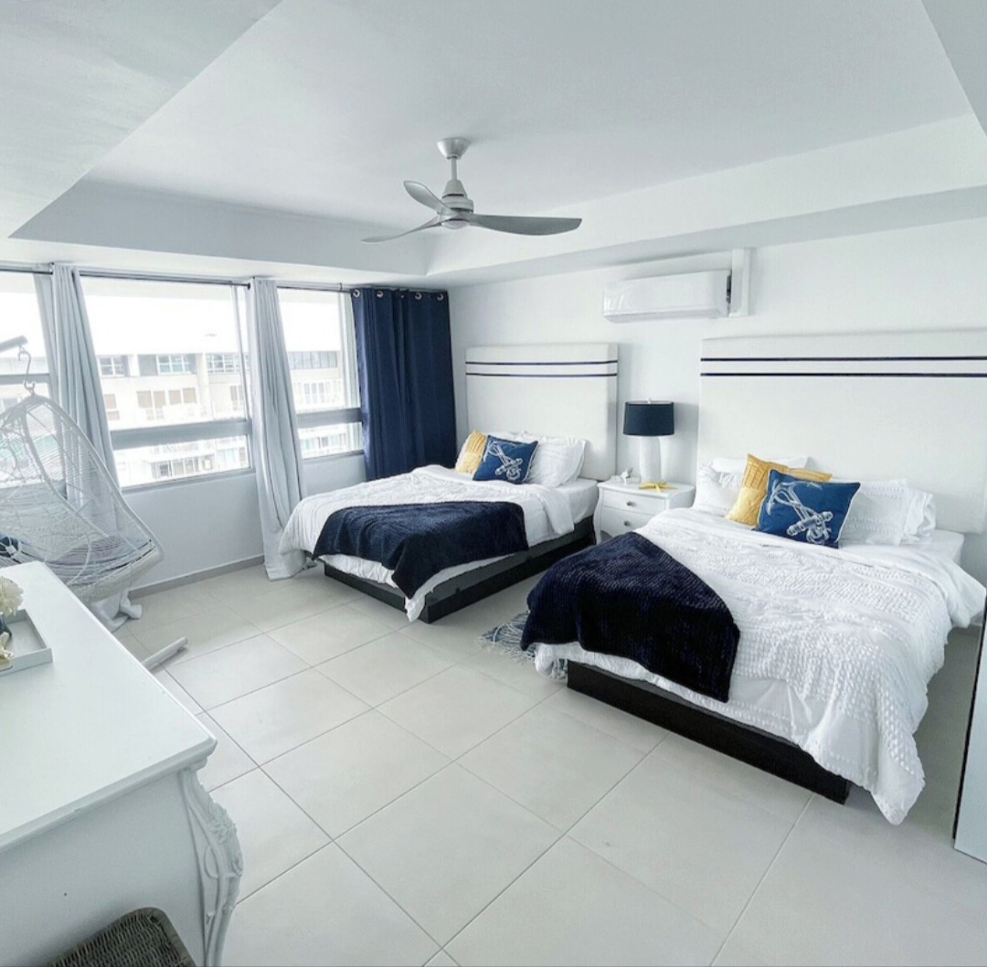 Een moderne hotelkamer met twee bedden, een plafondventilator, een bureau en een raam met gordijnen.