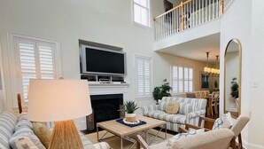 A spacious living room with a fireplace, a television, and a high ceiling with a balcony.