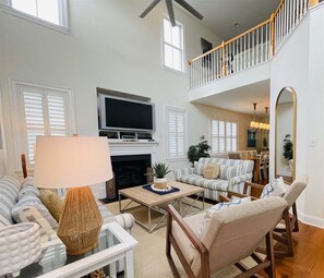 A spacious living room with a fireplace, a television, and a high ceiling with a balcony.