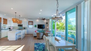Cozinha moderna com armários brancos, sala de jantar com mesa e cadeiras brancas, e uma grande porta de vidro deslizante que dá para uma varanda.