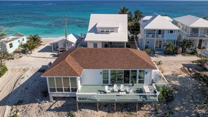 Um imóvel à beira-mar com uma casa grande, destacando um deck espaçoso com área de estar ao ar livre, piscina e vista para o oceano.