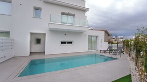 A modern two-story building with a swimming pool, a balcony with glass railings, and a view of the sea.