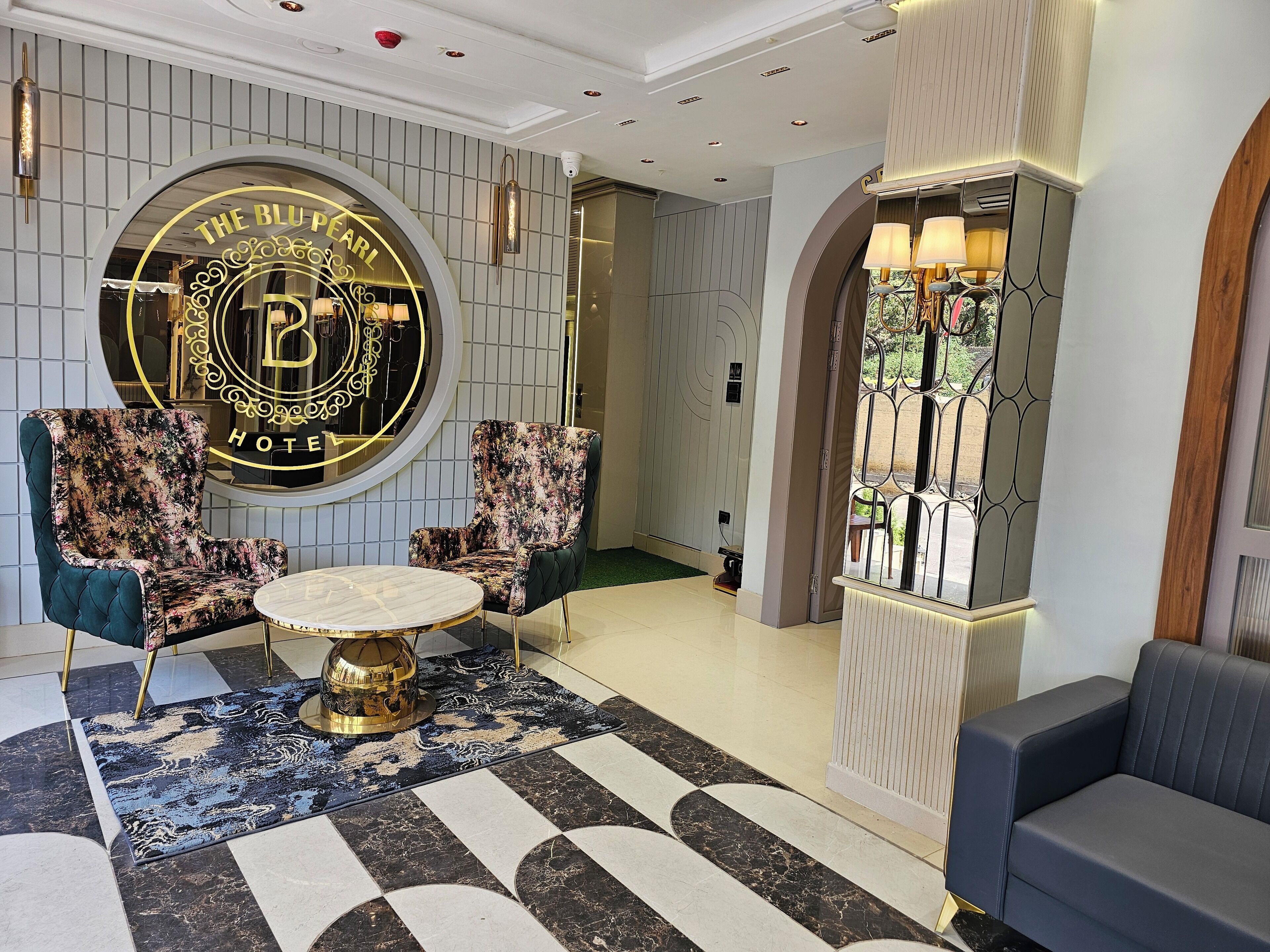 A lobby with a circular emblem, two upholstered chairs, a round table, and a patterned rug.