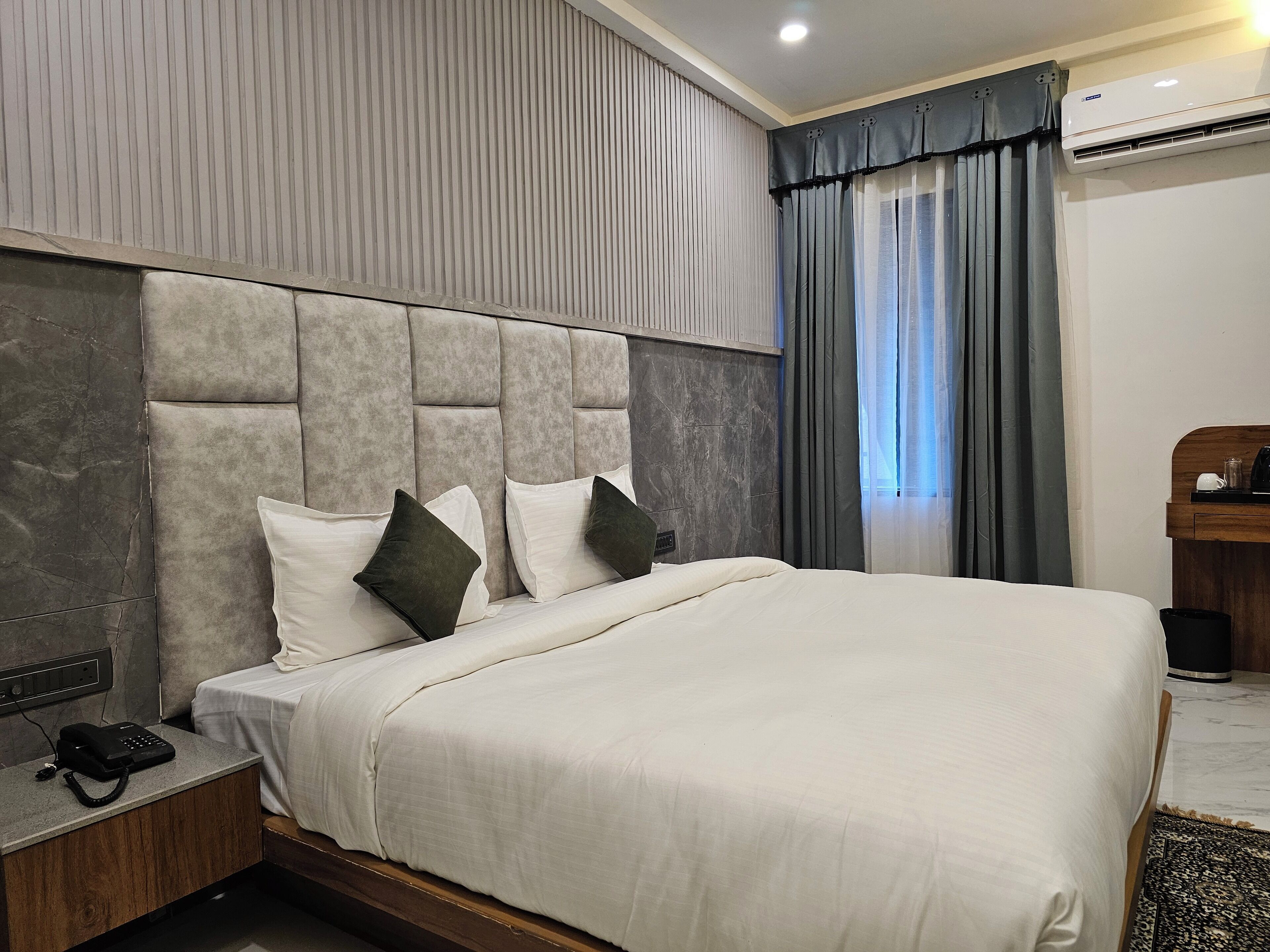 A modern hotel room with a large bed, a bedside telephone, and an air conditioning unit.