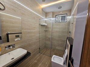 A modern bathroom with a large mirror, a sink, a toilet, and a glass-enclosed shower area. - The Blu Pearl (Gwalior)
