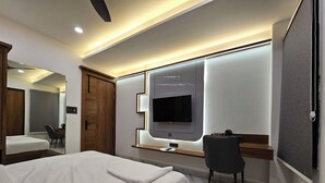 A modern hotel room with a large bed, a desk with a chair, a television mounted on the wall, and a mirror. - The Blu Pearl (Gwalior)