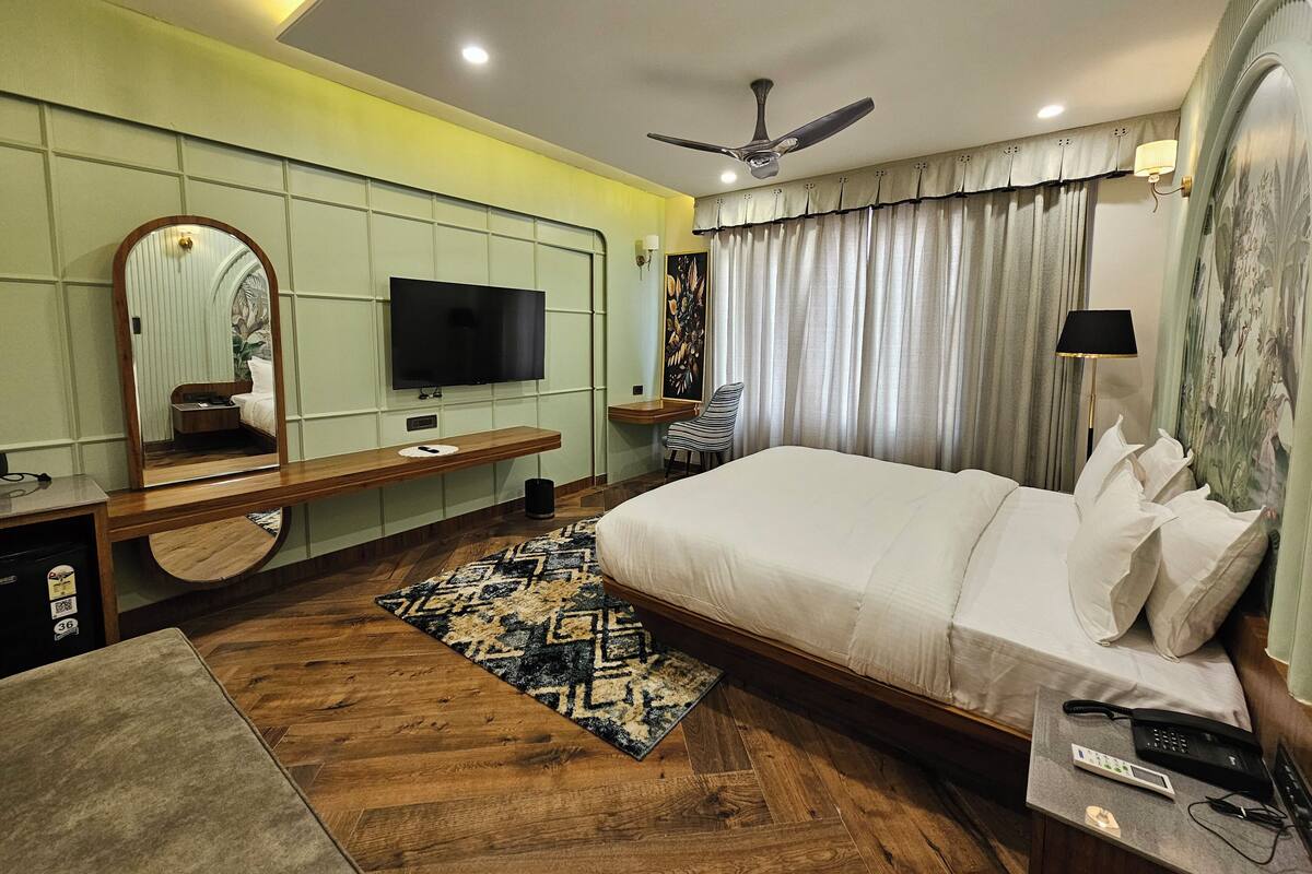 Una habitación de hotel moderna con una cama grande, un televisor de pantalla plana, un ventilador de techo y una mesita de noche con lámpara.
