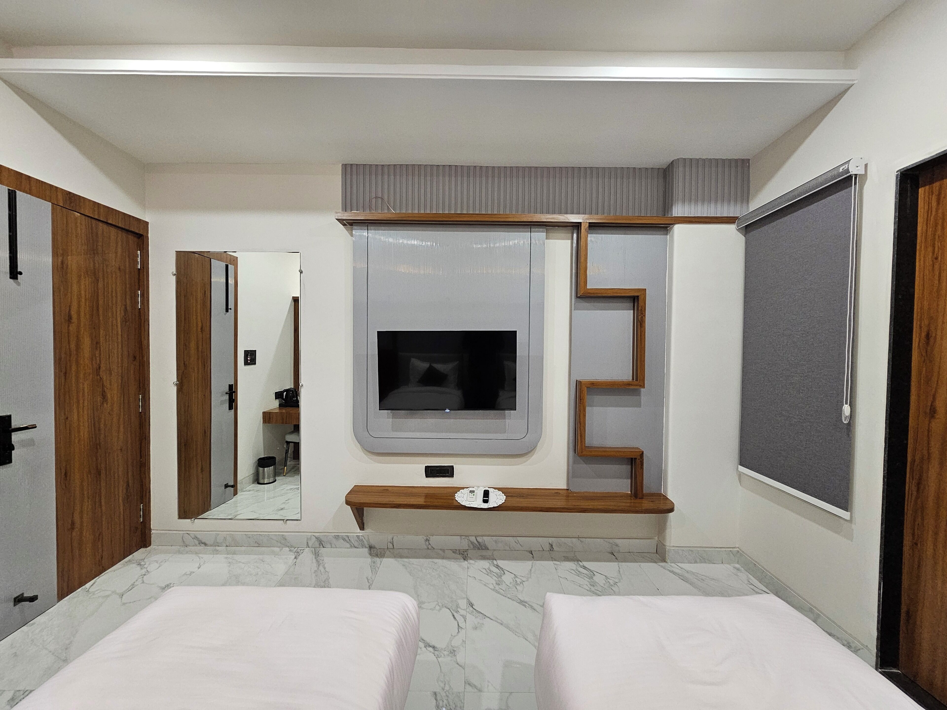 A hotel room with a large bed, a TV mounted on a wooden panel, a mirror, and a wardrobe.